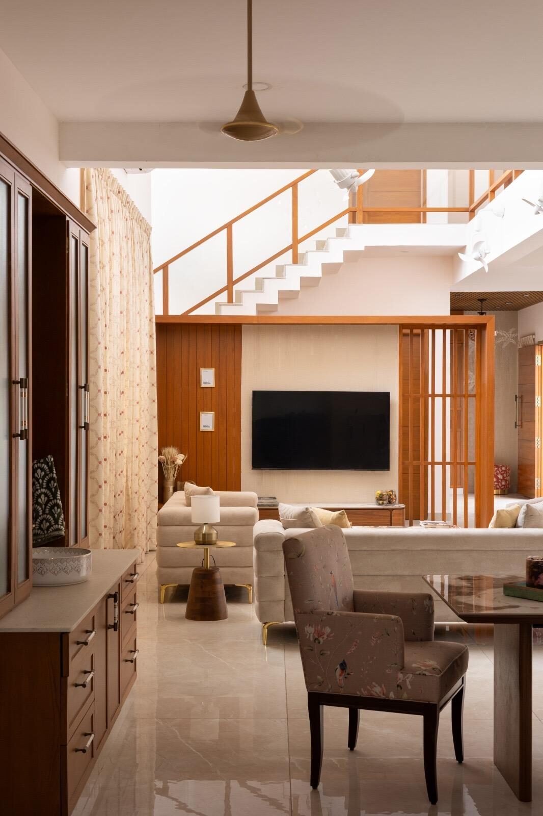 Double-height living room with a teak wood staircase railing, floral armchairs and warm ambient lighting